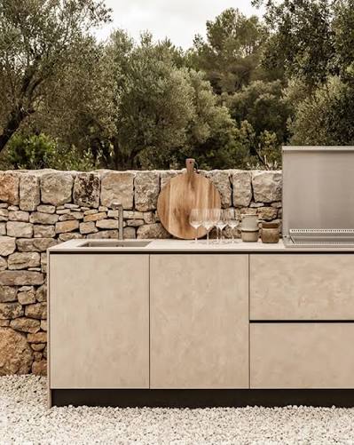 Cuisine d’été aux façades beige texturées avec évier et grill face à un mur en pierre